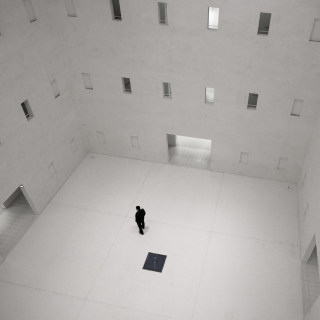 A man dressed in a  square lobby type place surrounded with many doors